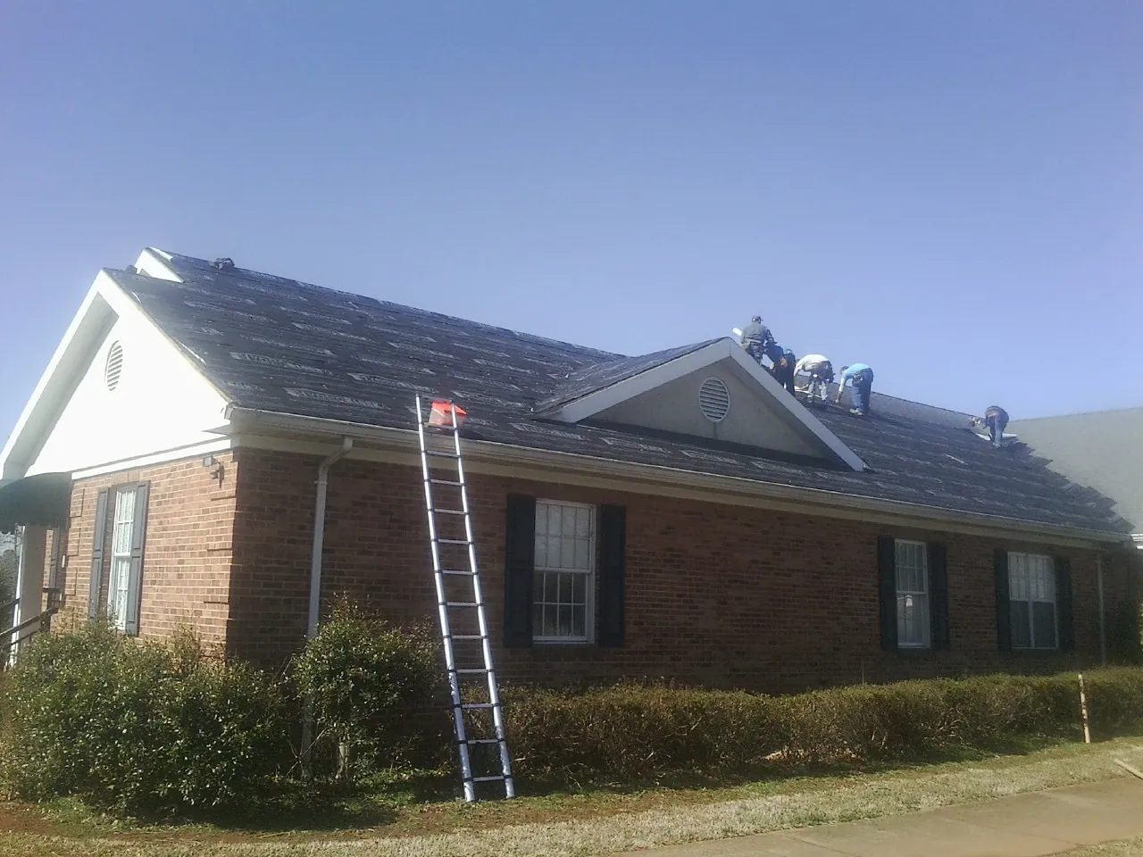 Crew tearing shingles off a brick ranch roof with a ladder set — Metal Roof Repair work by our crew in Lothian