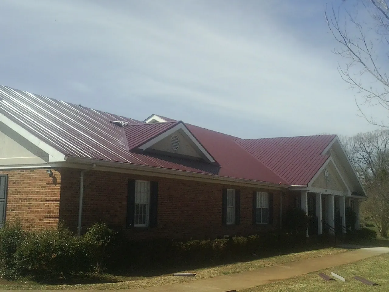 Red metal roof with gabled entries on a long brick building, from a Hail Damage Roof Repair job in Lothian