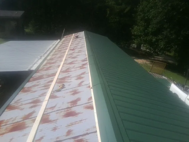 Old rusted panels beside newly installed green metal roofing — Wind Damage Roof Repair by Roofing Brothers in Lothian