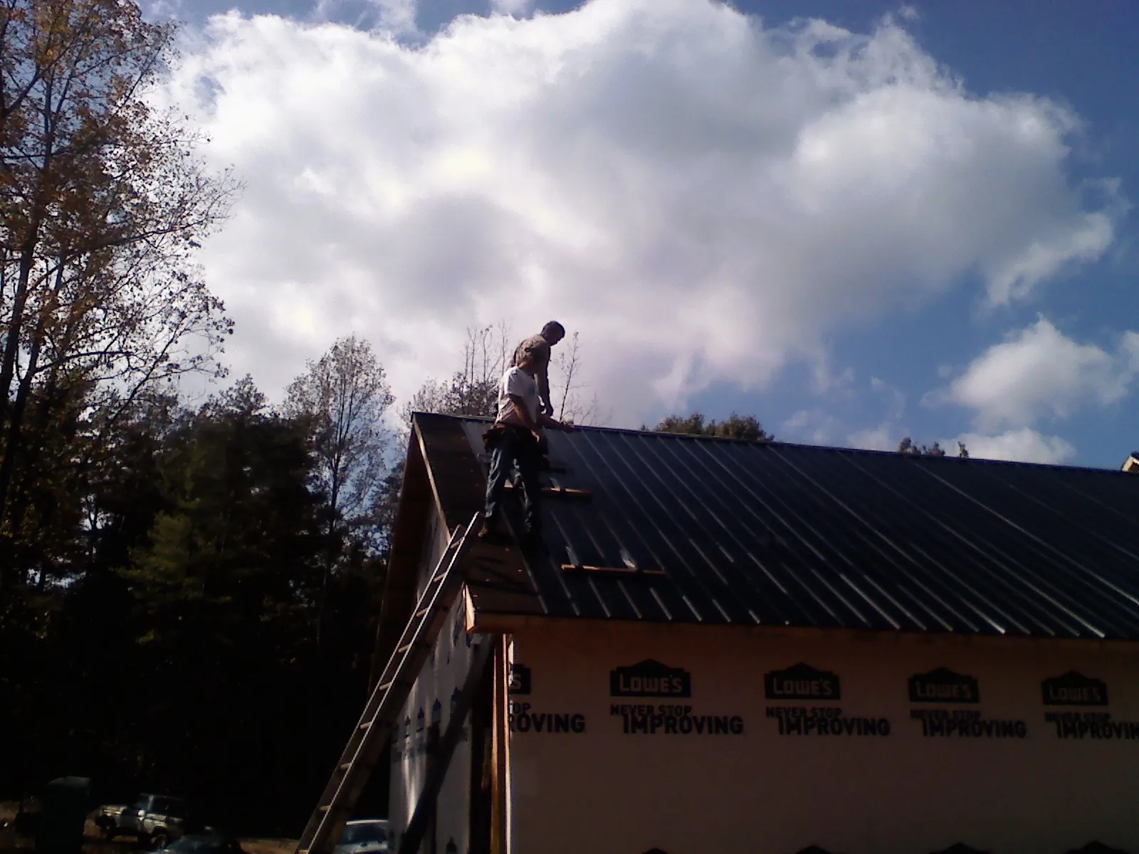 Roofer fastening dark metal panels high against a cloudy sky, from a Roof Inspection job in Lothian