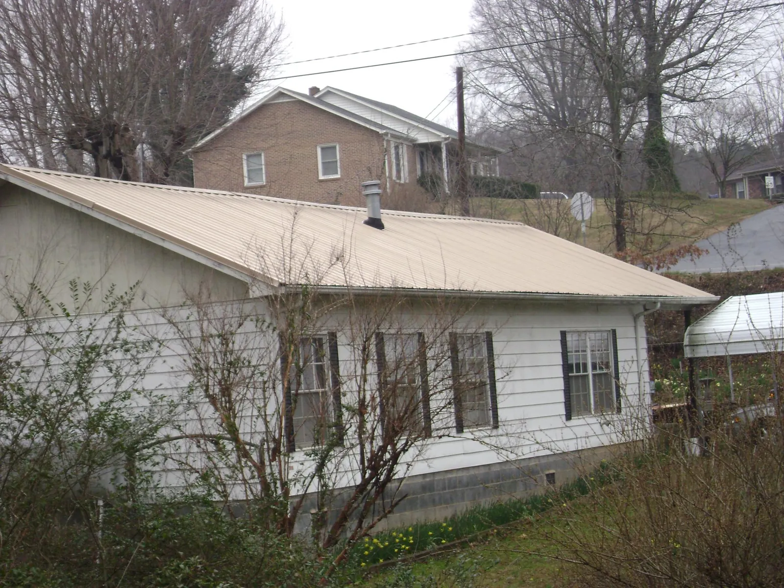 Tan metal roof on a white sided house set into a hillside — Commercial Roofing by Roofing Brothers in Lothian
